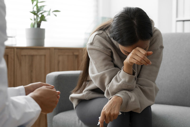 Woman sitting on a sofa with her head bowed and hand to her forehead in a counseling session