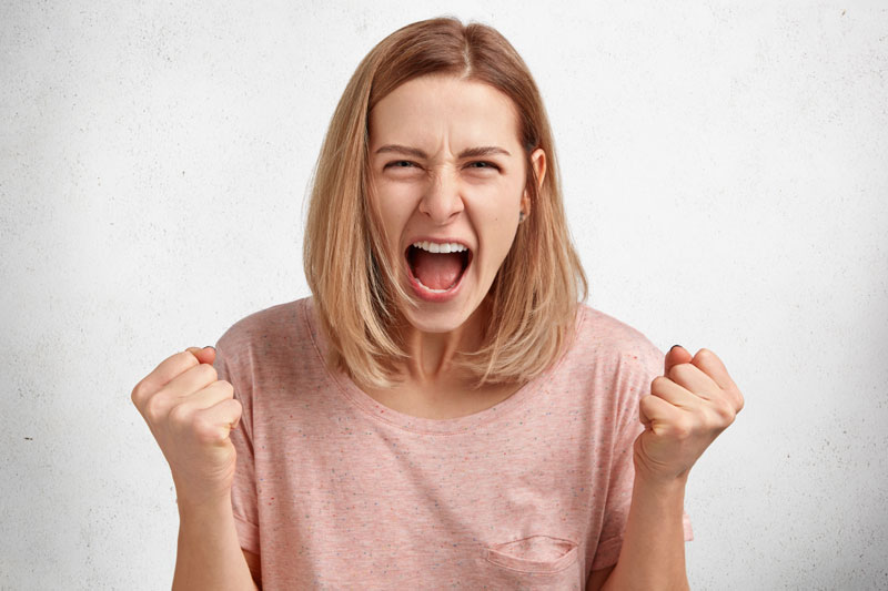 Young woman with blond hair shouting fists clenched in front of her expressing strong anger or excitement