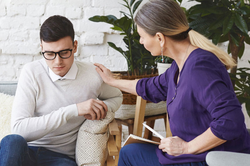 Therapist consoles a man during a counseling session placing a hand on his shoulder